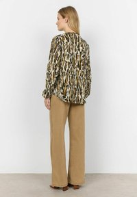 Long-sleeve blouse in a beige and green animal print, made of lightweight fabric, paired with high-waisted beige wide-leg pants and block-heel sandals.