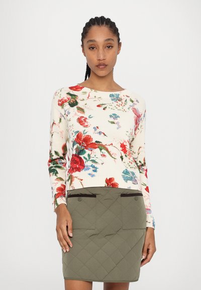 Pull en tricot floral avec une base crème, orné de fleurs rouges et bleues ; associé à une jupe matelassée verte avec des détails de poches.