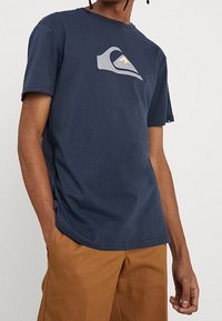 Marinblå bomulls-t-shirt med rund hals, korta ärmar och en grå bergsvåg-logotyp på bröstet; avslappnad passform, mjuk textur.