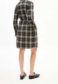 Abito a scacchi bianco e nero, con vita attillata, maniche lunghe, lunghezza al ginocchio, con una texture liscia. Indossato con scarpe nere slip-on.