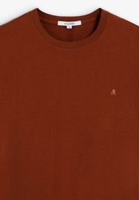 Camiseta de algodón marrón con un cuello redondo clásico, que presenta un pequeño logo bordado en el lado izquierdo del pecho. Textura suave con un corte holgado.