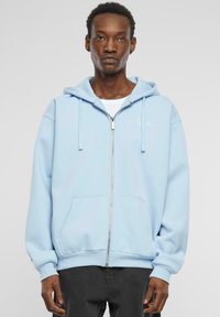 Hellblaue Zip-Hoodie mit Kapuze und Kordelzug, Fronttaschen und gerippten Bündchen. Weicher Stoff mit dezentem Logodetail auf der Brust.