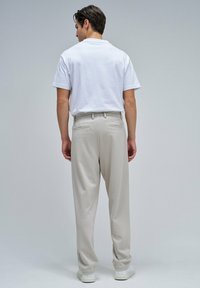 Pantalones beige para hombre, hechos de un material suave, con un corte relajado, bolsillos traseros y combinados con una camiseta blanca sencilla y zapatillas blancas.