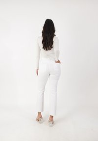 Top blanco de manga larga, jeans blancos de alta cintura, recortados en el tobillo, con bolsillos traseros. Sandalias de tacón transparente. Texturas simples y suaves.