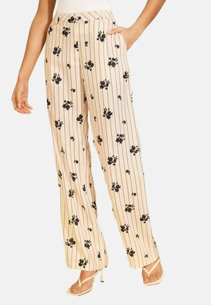 Beežid laia säärega püksid mustade vertikaalsete triipude ja lillemustriga, kantud beežide rihmikuga kõrgete kontsadega sandaalidega.