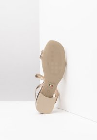 Sandalo metallico dorato con fasce incrociate, suola piatta beige, fondo texturizzato e dettagli di branding. Progettato per comfort e versatilità.