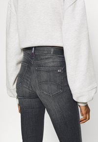 Jeans grigi scuri a vita alta con una classica texture in denim, dotati di una toppa con logo in vita e due tasche posteriori.