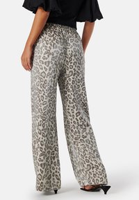 Wijdvallende broek van een lichtbeige stof, versierd met een grijze luipaardprint, elastische tailleband en subtiele glans.