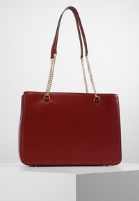 Punainen synteettinen käsilaukku, jolla on jämäkkä muoto, sileä pintakuvio, kaksipituinen kahva ja kullanväriset ketjusomisteet.
