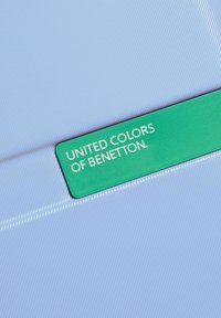Light blue textured surface with diagonal lines, featuring a green label displaying "UNITED COLORS OF BENETTON" in white text.
