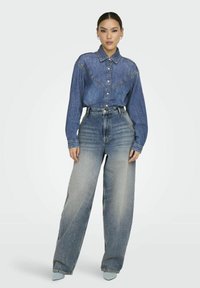 Camicia di denim con bottoni frontali, maniche lunghe e colletto a punta; abbinata a jeans azzurri a gamba larga con effetti sbiaditi.