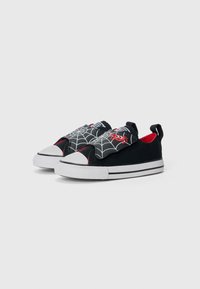 Melni audekla slip-on apavi ar baltām gumijas zolēm. Augšdaļā ir zirnekļa un tīkla dizains, sarkanie akcenti un cilpa aizmugurē.