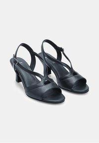 Décolleté in pelle nera con apertura sul davanti, design con cinturino T, dettagli ritagliati e un piccolo tacco a blocco per stabilità.