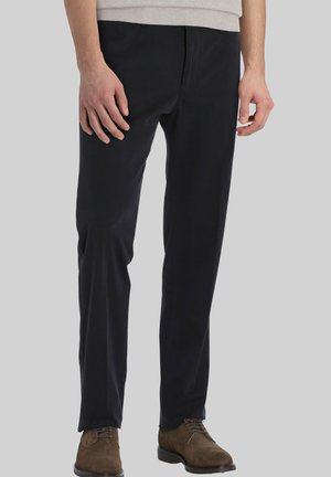 Zwarte slim-fit broek gemaakt van zacht katoen met een gladde textuur. Voorzien van voorzakken en riemlussen. Gecombineerd met bruine suède schoenen.