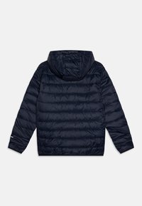 Námornícko modrá puffová bunda s kapucňou, prešívaný dizajn a dlhé rukávy. Obsahuje elastické manžety a zipsovú kapsu na ľavom rukáve.