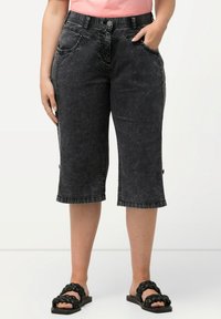 Mustat denim-capri-housut, joissa on haalistunut pinta, etutaskut, nappisulku ja tikkireunat. Yhdistetty mustiin liukusandaaleihin.