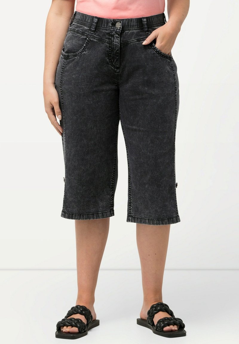 Mustat denim-capri-housut, joissa on haalistunut pinta, etutaskut, nappisulku ja tikkireunat. Yhdistetty mustiin liukusandaaleihin.