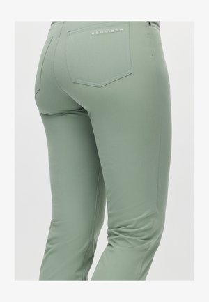 Lysegrønne, tætsiddende bukser lavet af glat stof. Har en baglomme med et påsyet logo og en subtil struktur i stoffet.