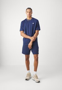 Maglietta a maniche corte blu navy e pantaloni corti coordinati, in misto cotone, con un piccolo logo sul petto. Sneakers color sabbia con dettagli bianchi e calze.