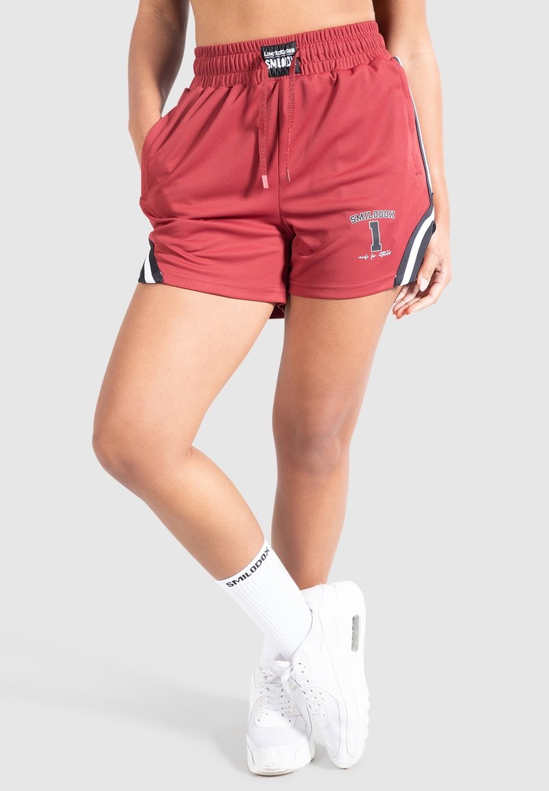 Red athletic shorts with an elastic waistband, drawstring, side black stripes, and printed logo. Worn with white ankle socks and sneakers.