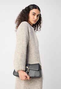 Black leather handbag with a textured finish, featuring a gold hardware clasp. The handle is held in a person's hand.