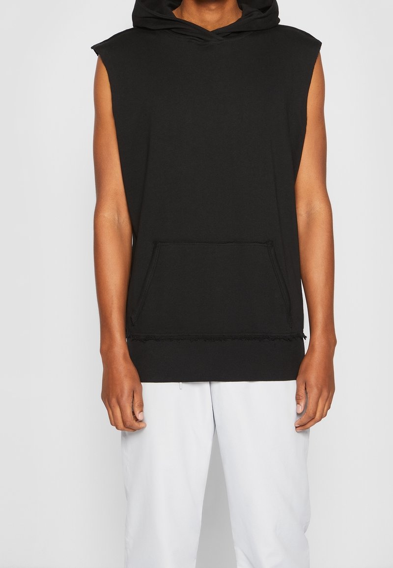 Black sleeveless hooded sweatshirt with a kangaroo pocket and raw-edge hem. Made of soft fabric with a relaxed fit and minimal detailing.