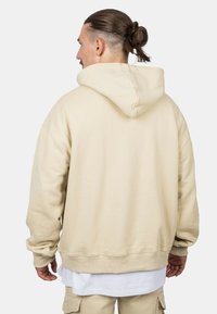 Beige oversized hoodie with a drawstring hood, ribbed cuffs, and a smooth texture, featuring a hem that slightly narrows at the waist.