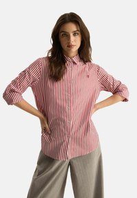 Czerwono-biała w paski koszula z guzikami, z kołnierzykiem, z długimi rękawami podwiniętymi. Małe haftowane logo na piersi.