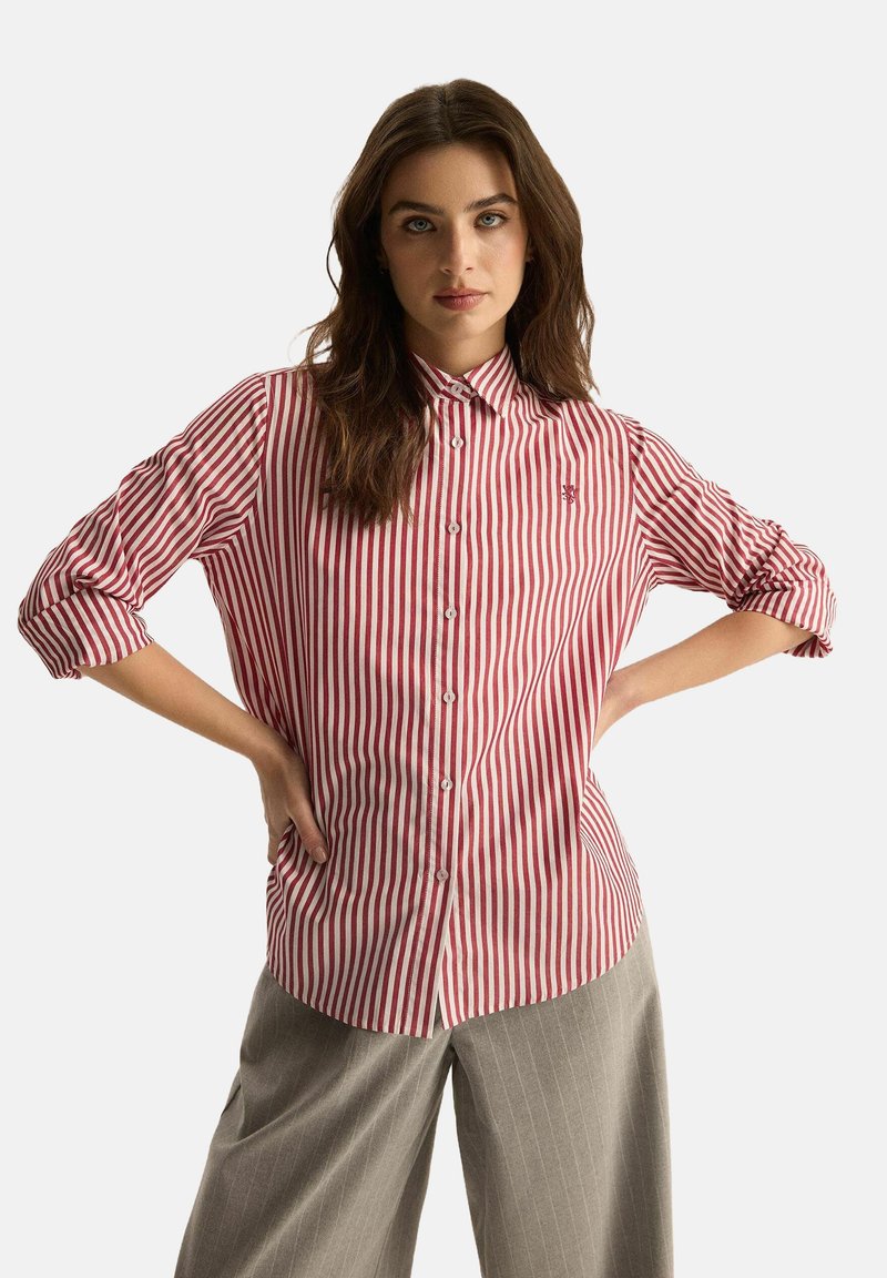 Czerwono-biała w paski koszula z guzikami, z kołnierzykiem, z długimi rękawami podwiniętymi. Małe haftowane logo na piersi.