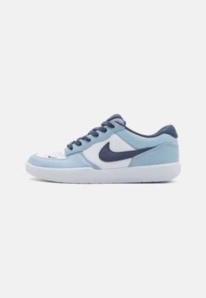 Basket basse Nike bleu clair, blanc et marine avec fermeture à lacets et semelle en caoutchouc, montrée de profil sur un fond uni.