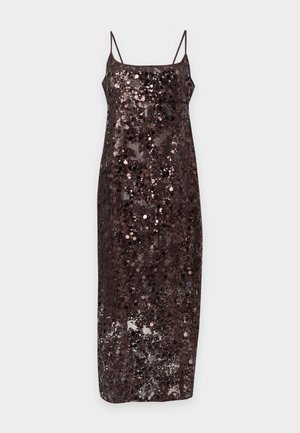Femme portant une robe midi noire sans manches à sequins avec des fines bretelles et des escarpins noirs à bout pointu, posant devant un fond uni.