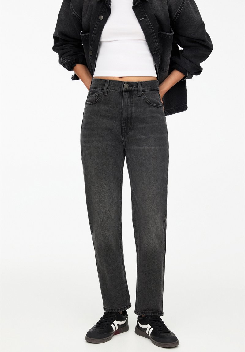 Svarta högmidjade jeans med avslappnad passform och blekt textur, kombinerat med en cropped vit topp och svarta sneakers med vita detaljer.