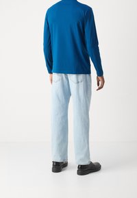 Blå långärmad skjorta i kombination med ljusblå, lösa jeans och svarta skor, vilket visar en avslappnad och stilig stil.