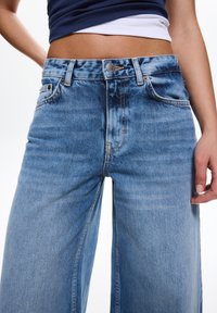 Jeans in denim blu a gamba larga con una finitura sbiadita, dotati di vita alta, cuciture visibili e tasche frontali. Chiusura con bottone in metallo.