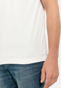Hvid bomulds T-shirt med korte ærmer, rund hals og lige kant; båret over mørkeblå denim jeans med subtil tekstur.