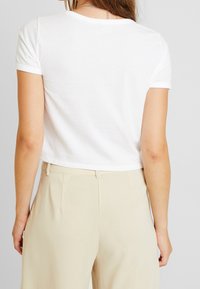 White cropped t-shirt with short sleeves, featuring a round neckline and a smooth, soft texture. Paired with high-waisted beige trousers.