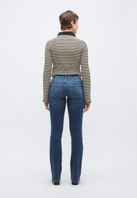 Ριγέ μπλούζα μακρυμάνικη με μαύρο γιακά, συνδυασμένη με μπλε flare τζιν παντελόνι με δύο πίσω τσέπες και μέτριο ξέπλυμα τζιν.