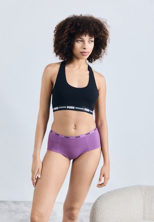 Sujetador deportivo negro con una cinta ancha de PUMA, combinado con braguitas hipster moradas que presentan una cinturilla con logo. Tela suave y elástica y diseño ajustado.