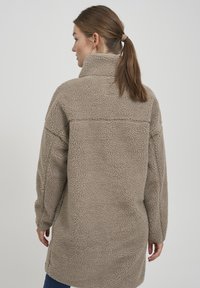 Taupe fleece jasje met een hoge kraag, oversized pasvorm, gestructureerd oppervlak en lange mouwen, met een eenvoudig ontwerp en zonder zichtbare hardware.