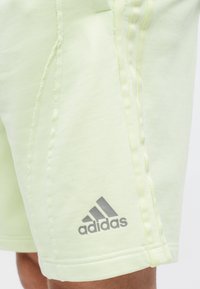 Șorturi Adidas de culoare verde deschis, cu o textură netedă, având branding gri și cusături contrastante pe laterale.