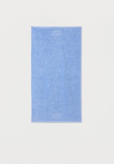 Modro pravokoten brisača z izbočenimi logotipi "HAY" blizu zgornjih in spodnjih robov, ravno položena na belem ozadju.