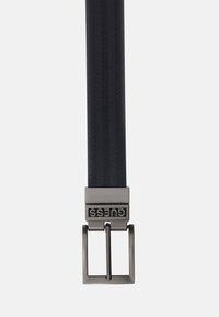 Sort vævet bælte med en chevronmønster, sølvfarvet metalspænde med præget brandlogo og rektangulær spændeform.