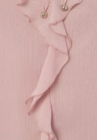 Rosa Stoffbluse mit Rüschendetail an der Vorderseite und zwei kleinen Metallknöpfen. Die Textur ist leicht zerknittert.