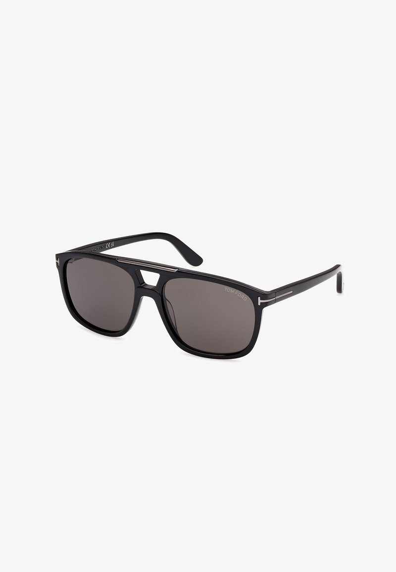 Lunettes de soleil rectangulaires noires avec des verres foncés et des branches fines, arborant un logo de marque discret dans le coin supérieur d'un des verres.