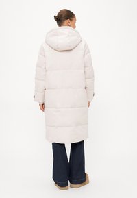 Lichtroze pufferjas met een capuchon, voorzien van horizontale stiksels en een middellange ontwerp, gecombineerd met uitlopende donkere jeans en tan-kleurige laarzen.