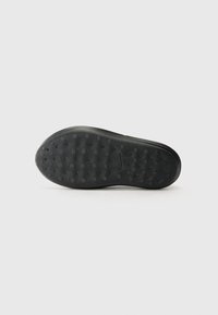 Black sneaker sole with textured surface, featuring circular and dotted patterns for grip. Material appears rubbery, with a smooth finish.