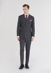 Szary dwurzędowy garnitur w kratę, biała koszula, czerwona muszka w kropki oraz poszetka. Czarne eleganckie buty dopełniają strój.