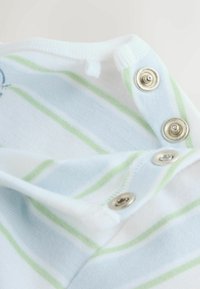 Gros plan sur un tissu blanc à rayures vertes et bleues avec trois boutons-pression en argent partiellement déboutonnés.