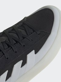 Čierne tenisky s textúrovaným vrchným materiálom, čiernymi šnúrkami a bielou gumovou podrážkou, ktorá má šikmé výrezy pre dizajnový detail.