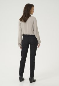 Black high-waisted skinny jeans with a smooth texture and back pockets, paired with a light gray blouse featuring soft draping and long sleeves.